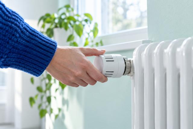 En hånd i blåt ærme justerer en hvid radiatortermostat ved en mintgrøn væg. AI-genereret temabillede.